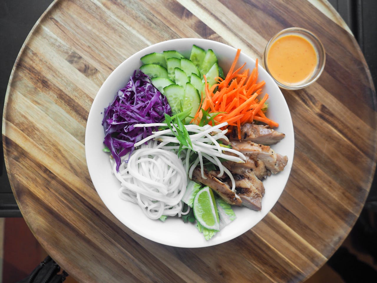 A colorful and healthy Vietnamese noodle bowl with fresh vegetables and grilled chicken on a rustic wooden table.