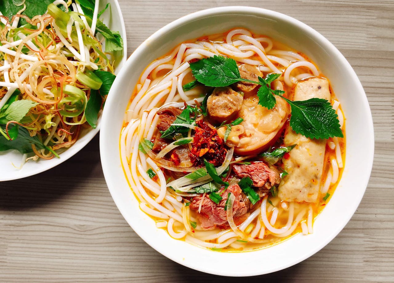 about-03 A colorful bowl of Vietnamese noodle soup with fresh herbs and vegetables.